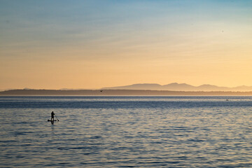 Silhouette of a man standing on a stand up paddle board in the sea during sunset
