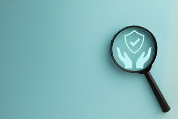 Hand holding insurance shield icon under magnifying glass with copyspace  representing security, protection, financial safety, risk management, and assurance for health, property, and life insurance.