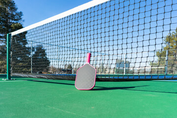 Low-angle view of pickleball paddle leaning against net of an outdoor pickleball court