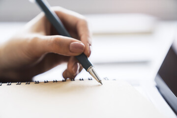 Closeup of female hand writing to notepad on blur background