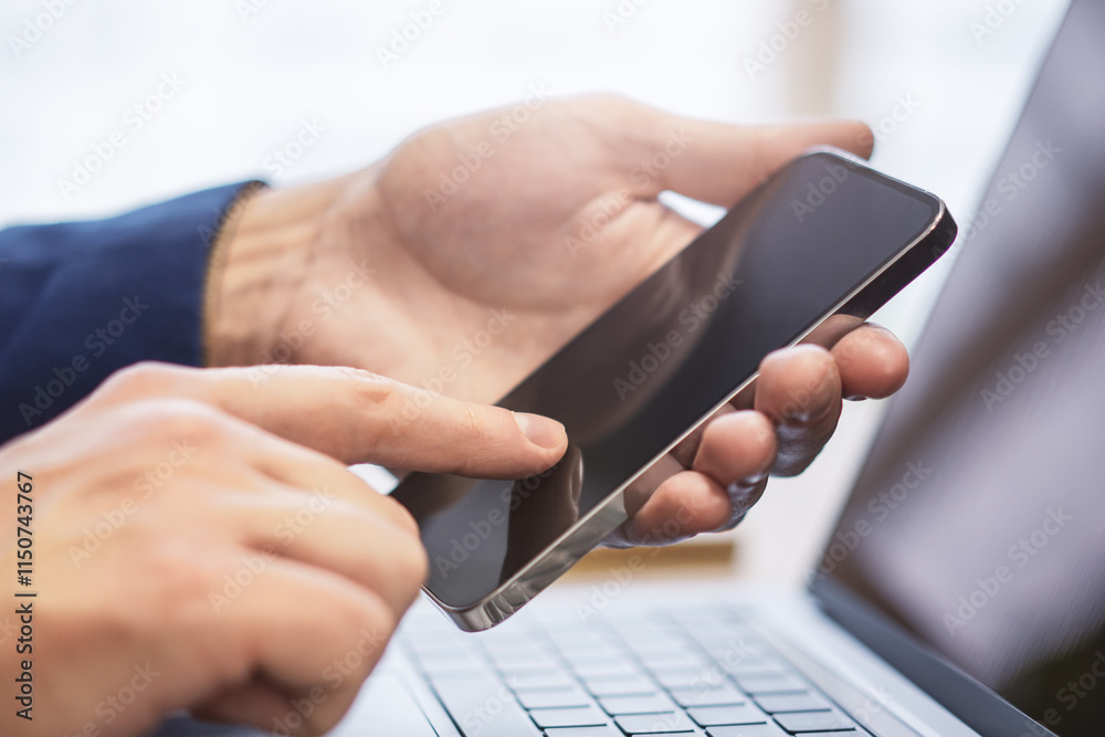 Poster detailed view of a man utilizing his modern smartphone at his workspace, laptop in the vicinity agai