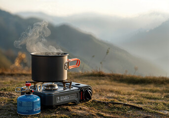 Steaming pot on portable gas stove during sunrise in mountains, creating a tranquil and adventurous camping scene