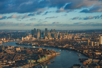 Fototapeta premium Aerial view of London's Canary Wharf skyline with modern skyscrapers. The River Thames reflects the warm glow of the setting sun during Christmas.