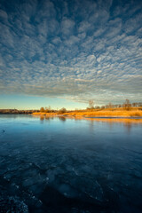 Naklejka premium Frozen sea at the winter ,morning on the pon, frozen water.Landscape with beautiful lake .Winter time , beautiful sunrise over the trees , smooth and big clouds in the sky, snow on the beach with reed