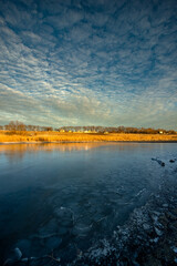 Frozen sea at the winter ,morning on the pon, frozen water.Landscape with beautiful lake .Winter time , beautiful sunrise over the trees , smooth and big clouds in the sky, snow on the beach with reed