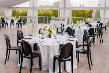 Served tables decorated with flowers in a restaurant on an open veranda with a fabric canopy. Preparations for receiving guests. Banquet in honor of the bride and groom
