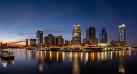 Fototapeta premium A panoramic view of a city skyline at dusk with glowing lights reflecting on the water