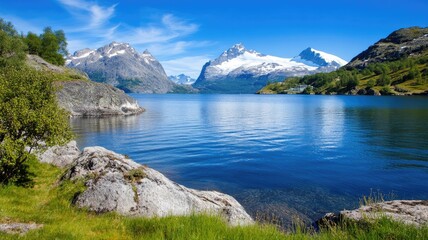 Serene lake with clear water, snowy mountains, and green hills under blue sky