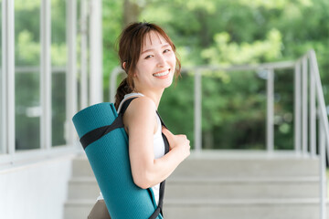 ヨガマットを持った健康的な女性（ヨガ講師・ヨギーニ）
