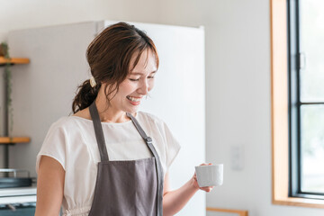 キッチン・ダイニングでコーヒーを飲むエプロン姿の若いアジア人女性
