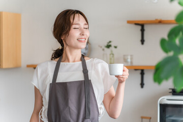 キッチン・ダイニングでコーヒー・紅茶を飲むエプロン姿の若いアジア人女性
