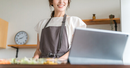 タブレットでアプリを使いレシピを見ながら料理するエプロン姿の女性
