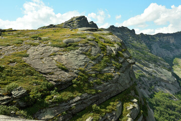 A fragment of a high rock with a steep cliff on top of a high mountain range on a cloudy summer day.