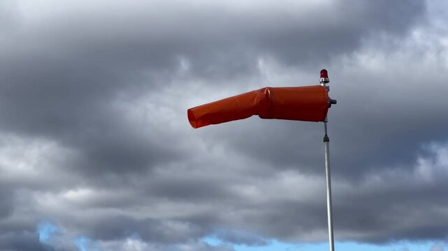 A video of a windsock, fully extended horizontally, vividly showing wind direction and force against a cloudy sky backdrop.