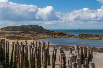 View of the coast of the city with wooden breakwaters in the foreground at low tide on a sunny summer day, Saint-Malo, Brittany, France