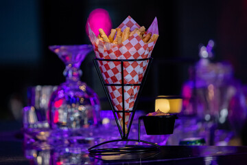 Crispy French fries served with salsa in a vibrant bar atmosphere with neon lights and reflections.