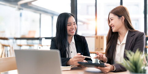 Two young Asian business woman talking, consulting and discussing  project idea presentation in the office.