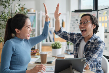 Two Asian startup entrepreneurs partner cheerful and high five together, successful marketing jobs...