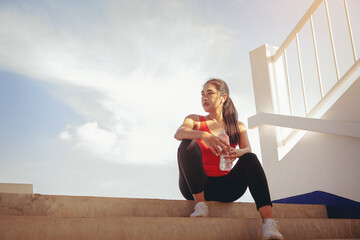 Tired runner woman with a bottle of electrolyte drink freshness after training outdoor workout at the stadium stairway.