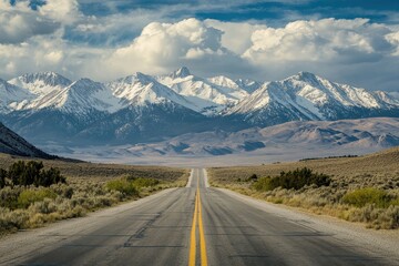 Fototapeta premium Scenic highway vanishing into snow-capped mountains under a partly cloudy sky.