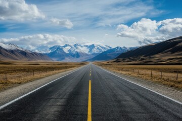 Open road leading to snow-capped mountains under a partly cloudy sky.