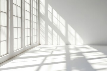 Obraz premium Sunlight streams through large window in a minimalist white room, casting shadows on the floor and wall.