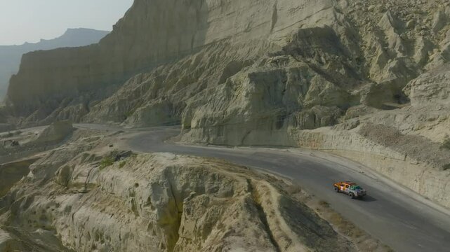 Breathtaking aerial view capturing a vehicle navigating the winding road through the dramatic canyons of buzi pass along the scenic makran coastal highway in balochistan, pakistan, drone pulling out