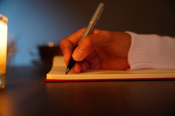Woman's hand writing in a journal with candle light at night concept background