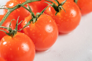 A group of bright, red cherry tomatoes with fresh stems attached, covered in dewdrops.