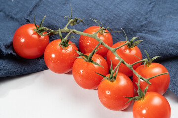 A group of bright, red cherry tomatoes with fresh stems attached, covered in dewdrops.