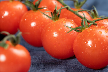 A group of bright, red cherry tomatoes with fresh stems attached, covered in dewdrops.