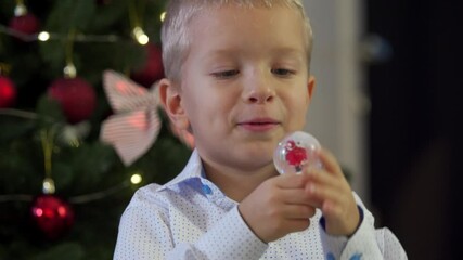 Happy child holding snow globe with figurine of Santa Claus. Smiling face of little boy near Christmas tree. Merry Christmas and Happy New year winter holidays.