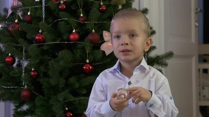 Happy child holding snow globe with figurine of Santa Claus. Smiling face of little boy near Christmas tree. Merry Christmas and Happy New year winter holidays.