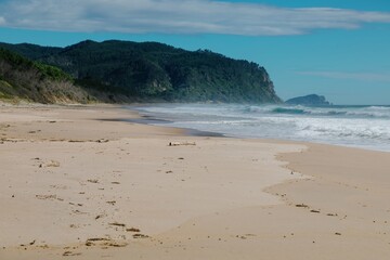 Tranquil beach scene with crashing waves, lush green hills, and a clear sky. Coastal beauty....