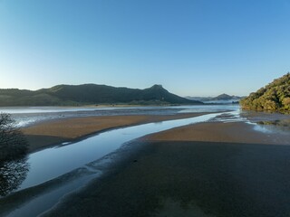 Fototapeta premium Tranquil coastal estuary at low tide. Calm waters reflect the sky and surrounding hills. Peaceful morning light. OPOUTERE, COROMANDEL PENINSULA, NEW ZEALAND