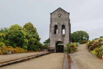 Ruined tower, overgrown with greenery, in a park. A path leads to the structure. MARTHA MINE, WAIHI, COROMANDEL PENINSULA, NEW ZEALAND