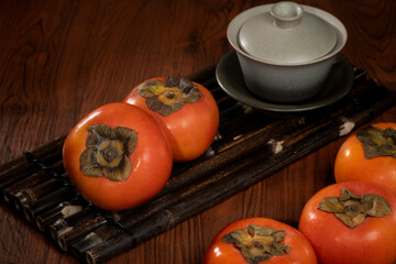 A rustic wooden tray filled with vibrant, ripe persimmons, their orange skin smooth and glossy.