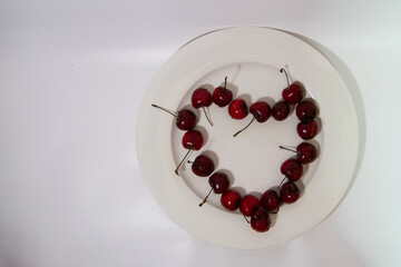 Red fresh cherries on a big white plate, heart shaped