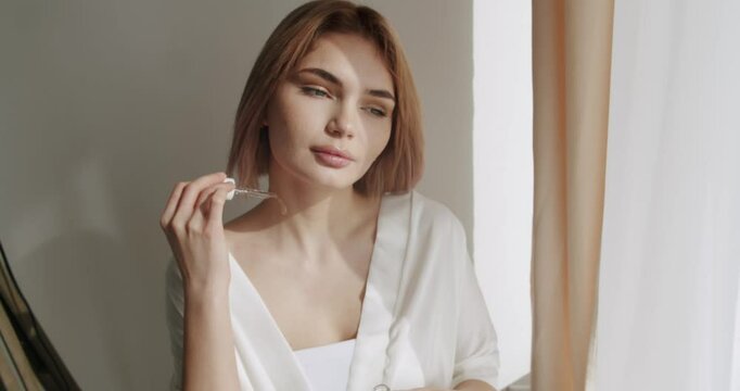 Woman dropping moisturizer with pipette on the shoulder and massaging. Woman applying serum. Anti aging or glowing skin. Young woman applying rejuvenating serum on her body.