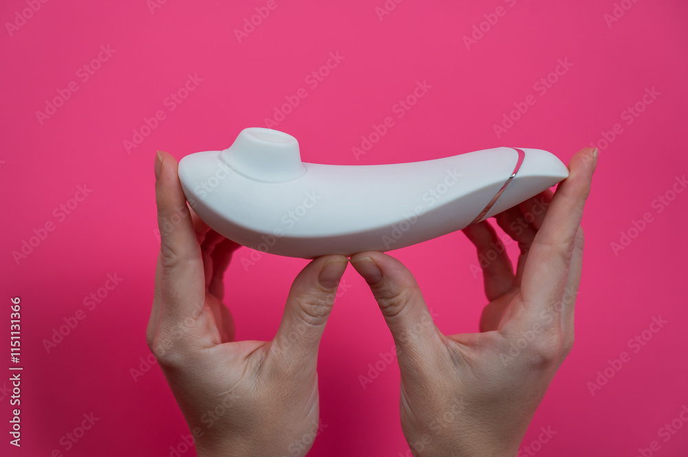 Wall mural Woman holding white vacuum clitoral vibrator on pink background. 