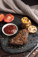 Roasted pork steak on black stone board over dark background. With tomato, sauce and fried potato