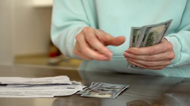 Woman counts us dollar banknotes on a table, surrounded by receipts. The scene captures the meticulous handling of cash, reflecting financial management and budgeting practices