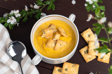 Fresh spicy organic creamy pumpkin soup in white bowl on wooden table with bread crackers. Top view