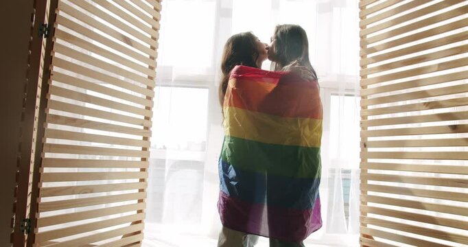 Couple, Lgbt and lesbian women at home. Embrace, smile and holding each other with flag. Love and kiss, LGBTQI. Romance and portrait of lesbian couple enjoying. LGBT rights, Lesbian family.