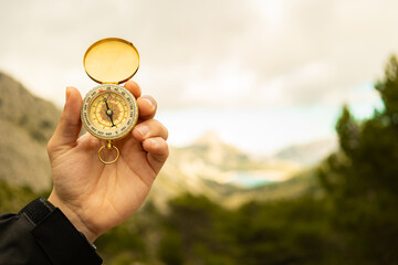 Male hand holding a compass on the mountain with grey clouds in the background, orientation in nature © Answer 7