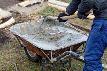 A man is shoveling cement into a wheelbarrow