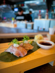 Raw Japanese Beef Sushi on a wood tray with soy sauce, wasabi and pickled ginger on the side with the chef in the background kitchen