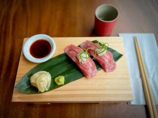 Raw Japanese Beef Sushi on a wood tray with soy sauce, wasabi and pickled ginger on the side