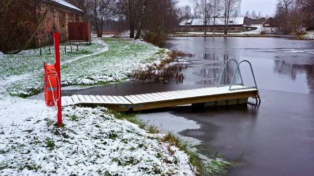 Frozen lakefront with wooden pier, lifebuoy, and snow-covered ground