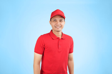 A cheerful Asian delivery worker in a red uniform and cap stands against a blue background, showcasing a friendly and professional demeanor ideal for customer-focused services.